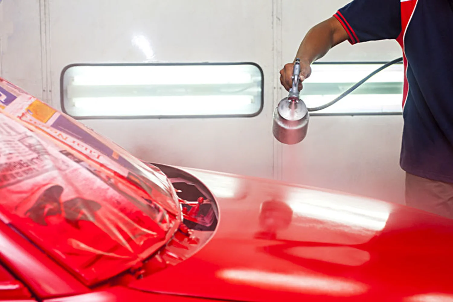 Spray painter applying red paint to a car panel inside a spray booth at an automotive workshop in Hobart