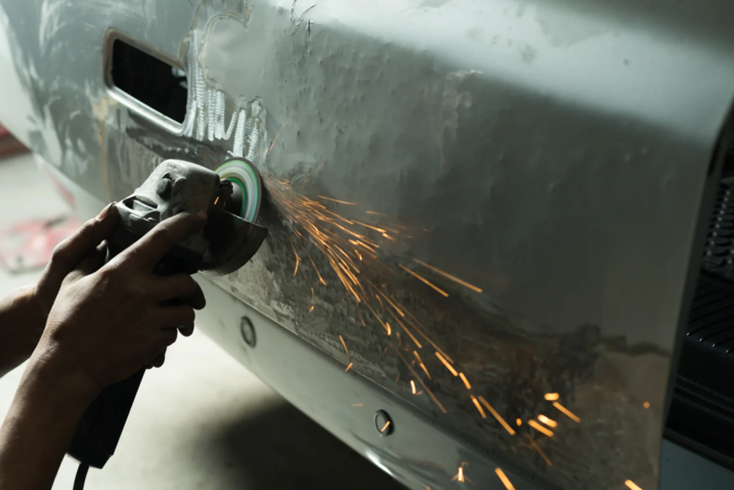 Technician using an angle grinder on a car panel during smash repairs at a workshop